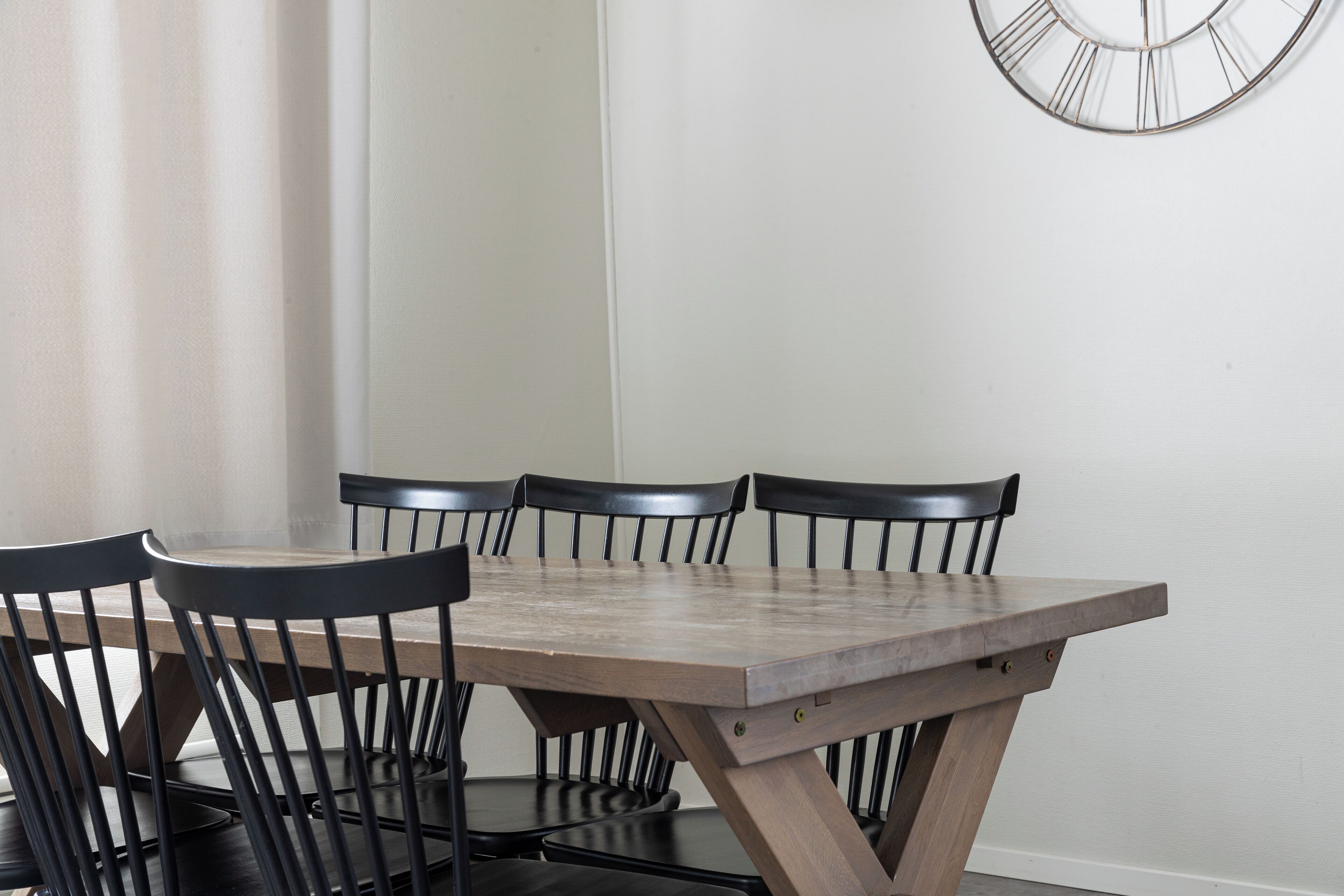 Une table à manger avec six chaises, une horloge au mur et une fenêtre avec des rideaux.