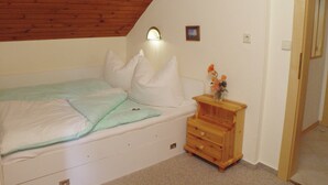A bedroom with a sloped ceiling, a bed with pillows, a nightstand with a vase, and a small picture on the wall. - Summer Vacation at Nassfeld (Hermagor-Pressegger See)