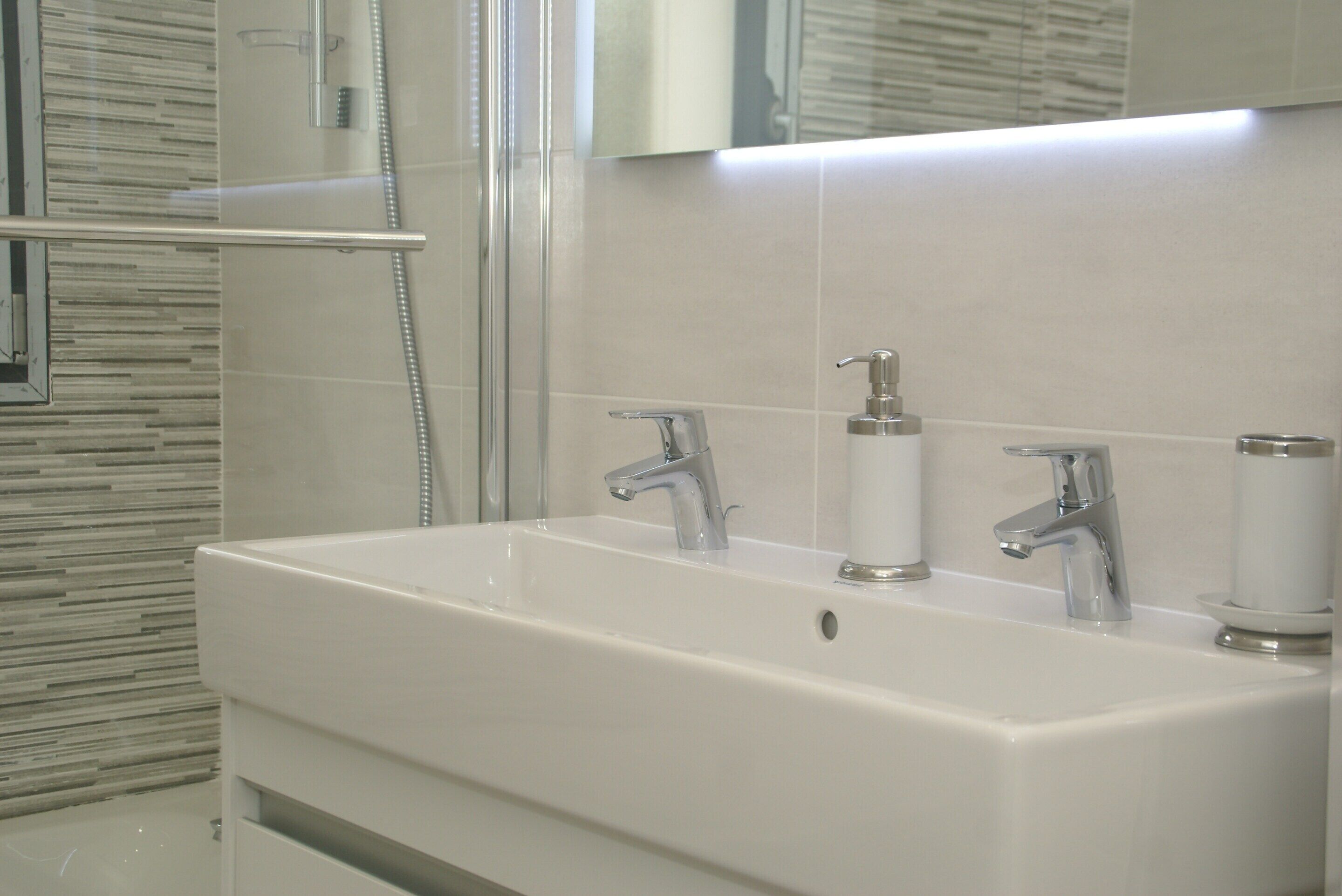 Un baño moderno con un lavamanos blanco, dos grifos y un box de ducha de vidrio.