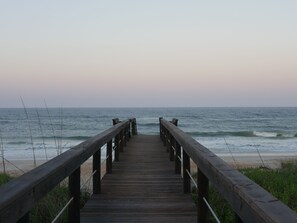 A wooden boardwalk leading to a beach with waves in the background.