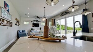 A spacious living area with a large island table, a ceiling fan, and a view of the outdoors. - Island Charm, Luxury Location & Pet Friendly (Holmes Beach)