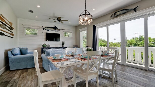 A dining area with a white table set for four, a ceiling fan, and a chandelier. - Island Charm, Luxury Location & Pet Friendly (Holmes Beach)