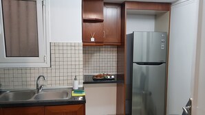 A kitchen with a stainless steel refrigerator, a sink with a faucet, wooden cabinets, and a tiled backsplash. - "Your Home @Acropolis Museum" by YHA (ΑΘΗΝΑΙΩΝ)