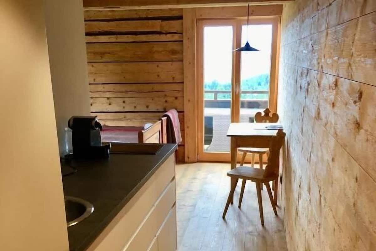 Una cocina estrecha con paredes y piso de madera, que conduce a un comedor con una mesa y sillas.
