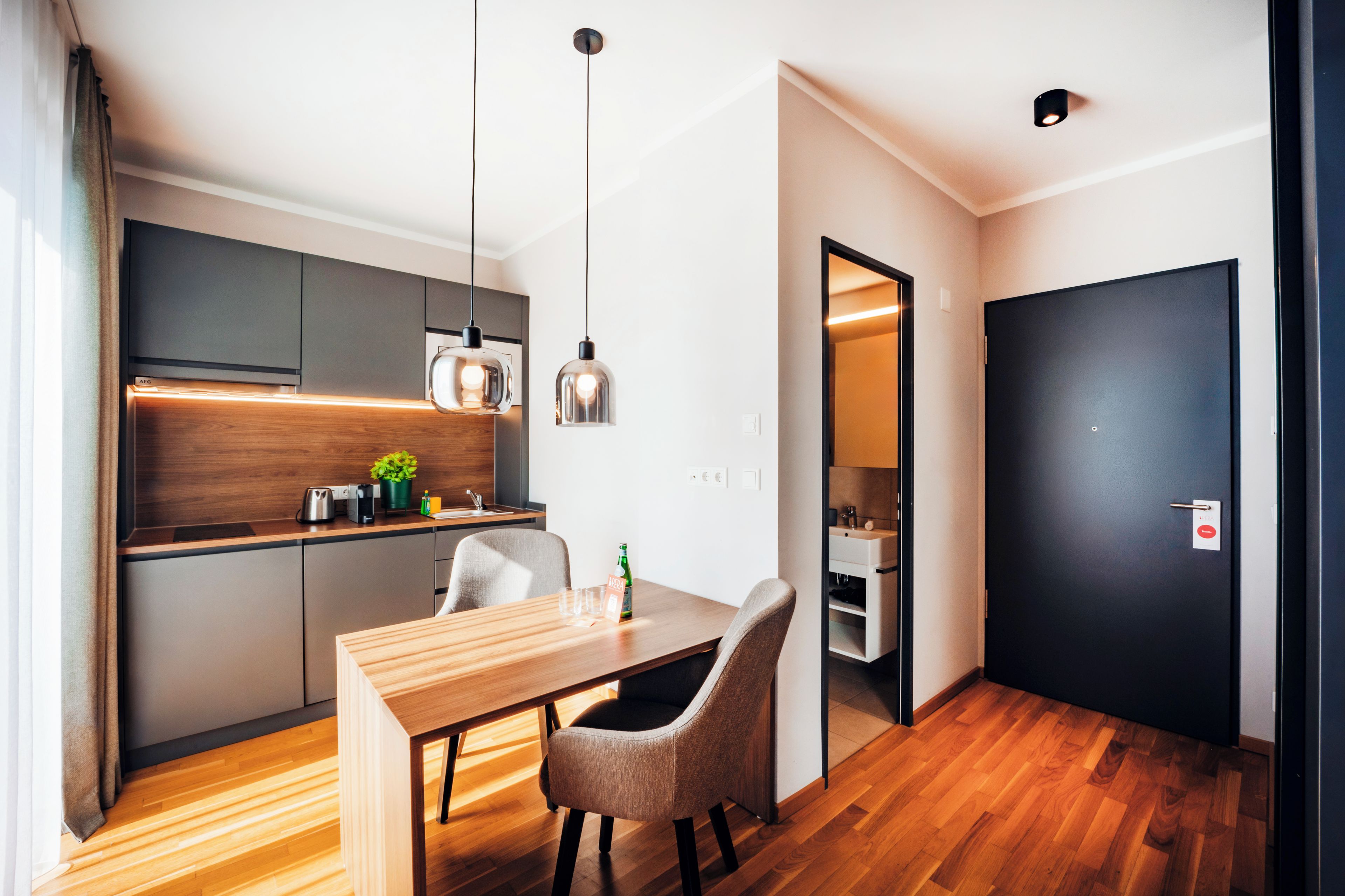 Una cocina moderna con encimera de madera, una mesa de comedor con sillas e iluminación colgante.