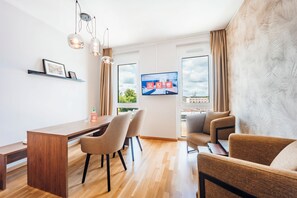 A modern living room with a wooden dining table, two chairs, a sofa, and a television mounted on the wall.
