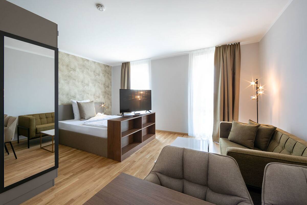 A modern hotel room with a large bed, a TV, a sofa, and a dining table.
