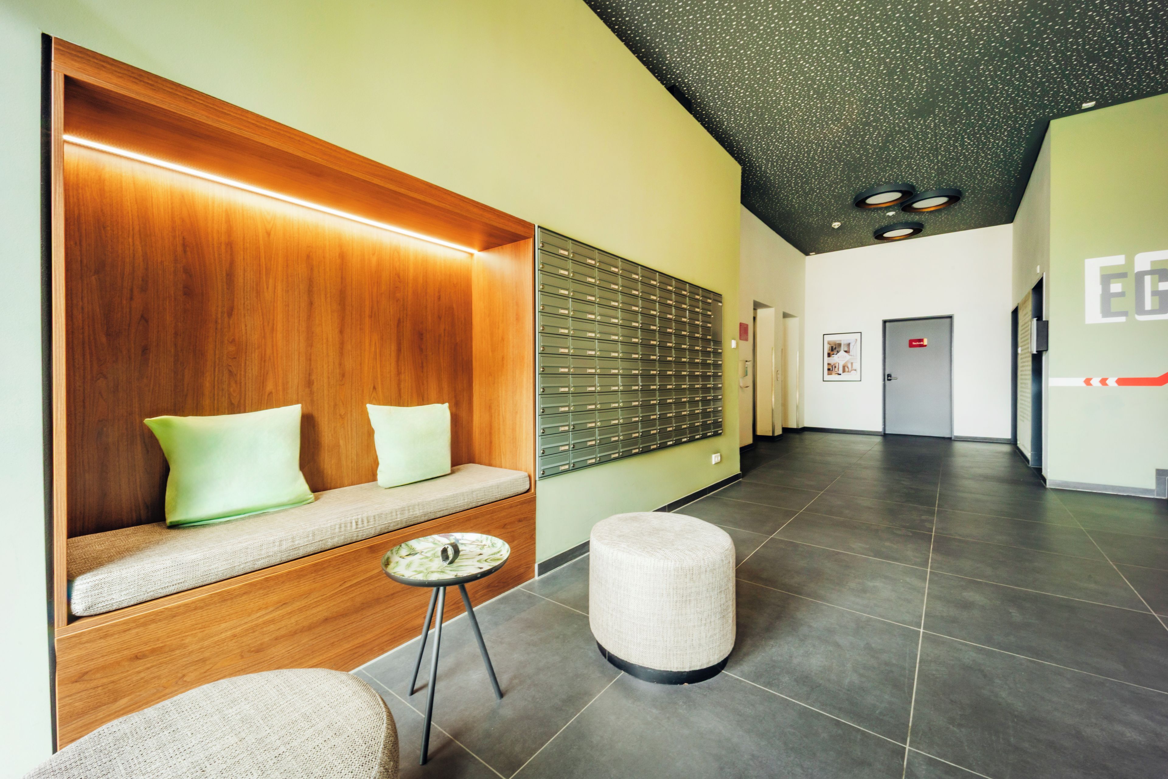 Un vestíbulo moderno con un banco de madera, un buzón empotrado en la pared y piso de baldosas.