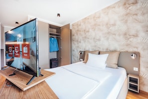 A modern hotel room with a bed, a television, a wardrobe, and a headboard with a textured design. - Brera Serviced Apartments Ulm (Ulm)