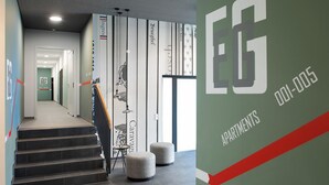 Een modern interieur met een trap, een muur met verticale strepen, en een bordje met de tekst 'EG Apartments 001-005'.
