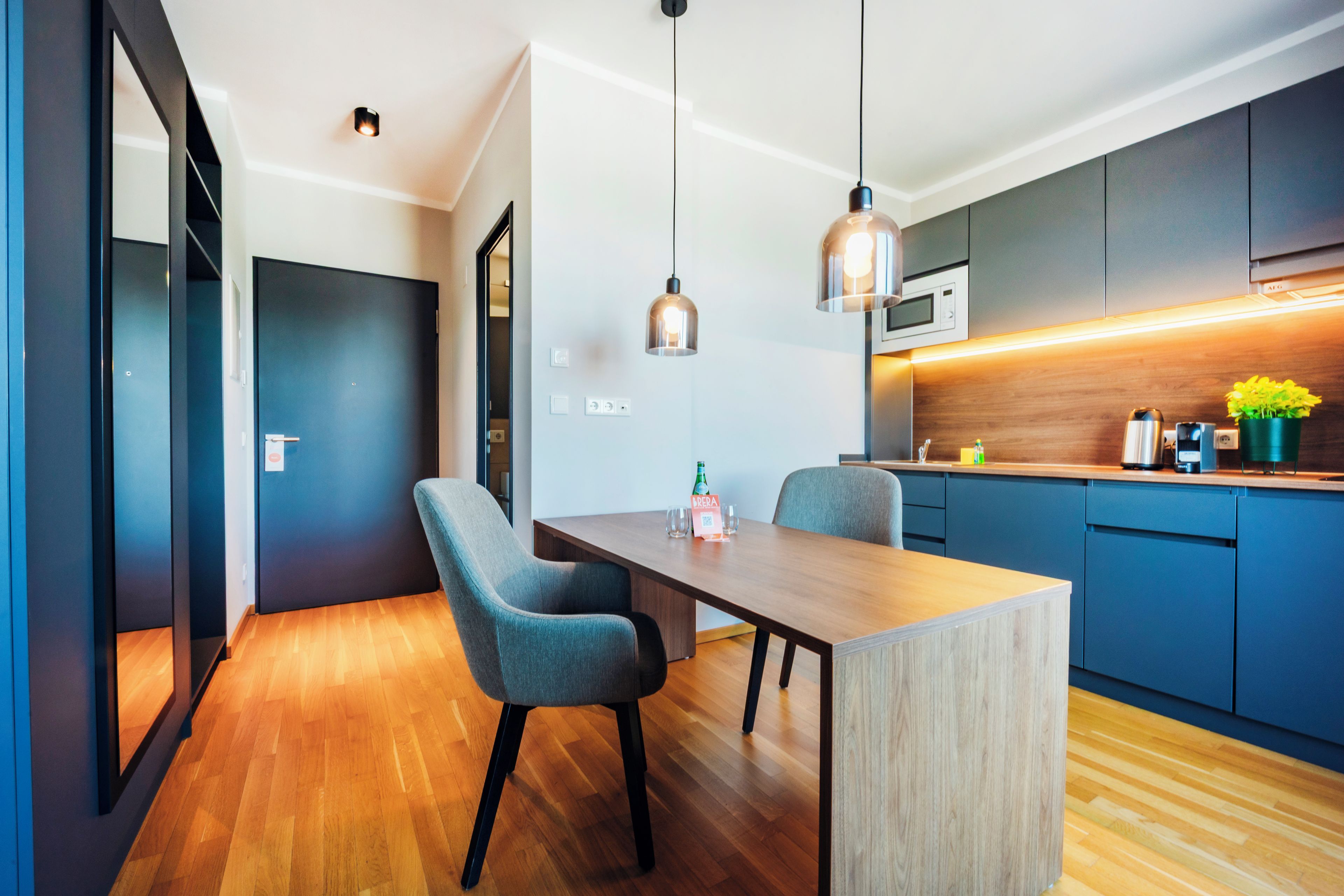 Una cocina moderna con una mesa de madera, dos sillas, lámparas colgantes y un microondas.