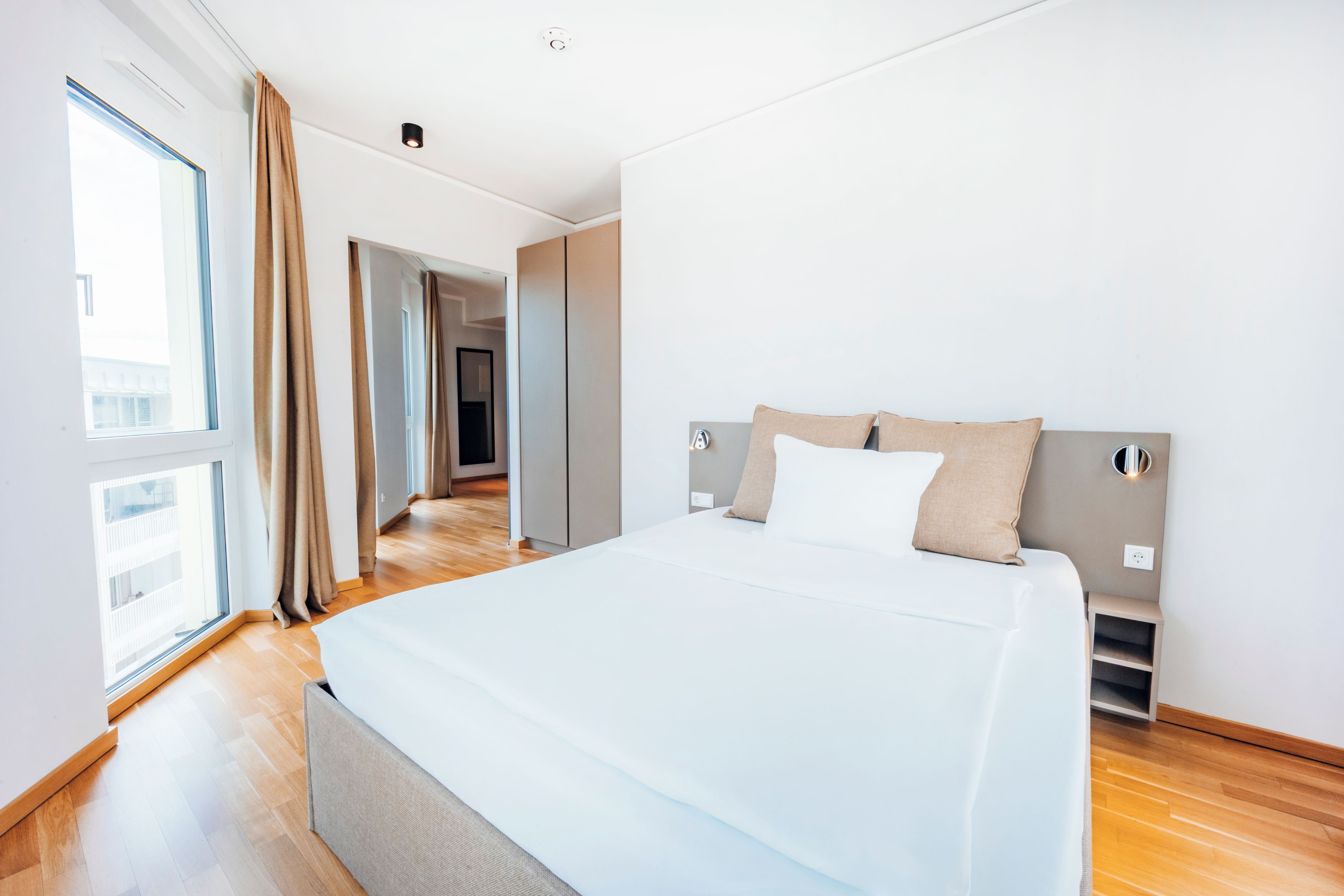 A modern bedroom with a large bed, a view of the city, and a walk-in closet.