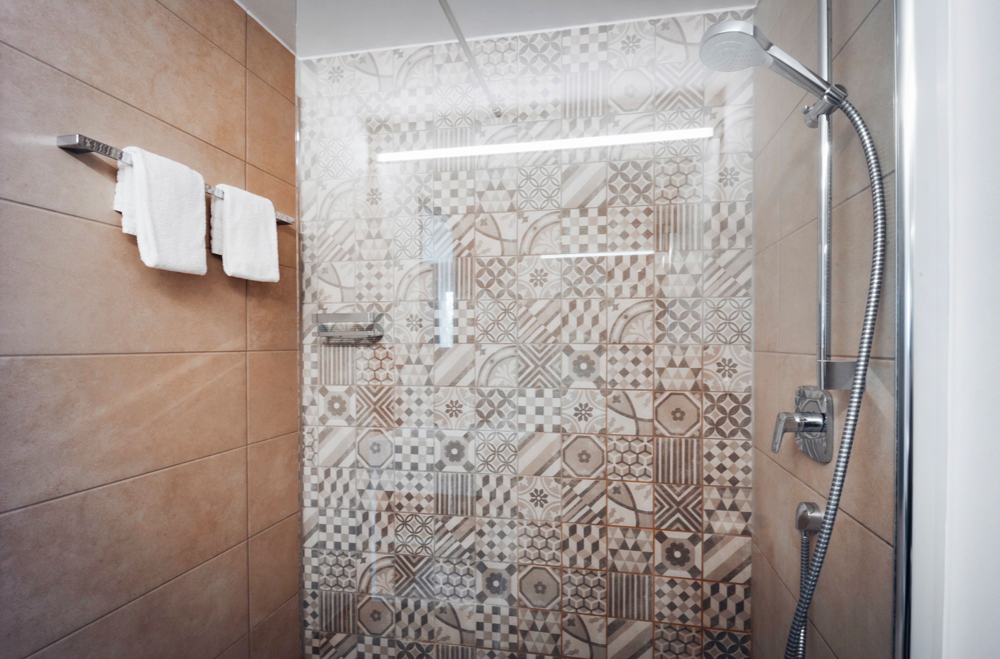 Una ducha con pared de azulejos estampados, un perchero con dos toallas y un cabezal de ducha manual.