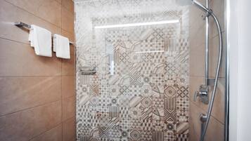 Una ducha con pared de azulejos estampados, un perchero con dos toallas y un cabezal de ducha manual.