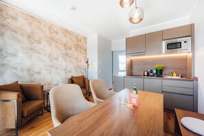 A modern kitchen with a microwave, a coffee machine, and a sink. There is a dining table with chairs and a bottle of beer.
