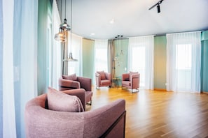 Un vaste espace de vie agrémenté de meubles modernes, de grandes fenêtres et d’un plancher en bois.