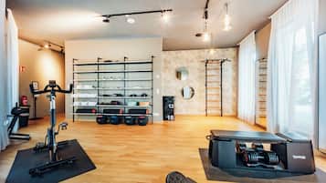 Ein Fitnessraum mit Trainingsgeräten, einem an der Wand befestigten Gewichtsheberregal und einer Klimmzugstange.