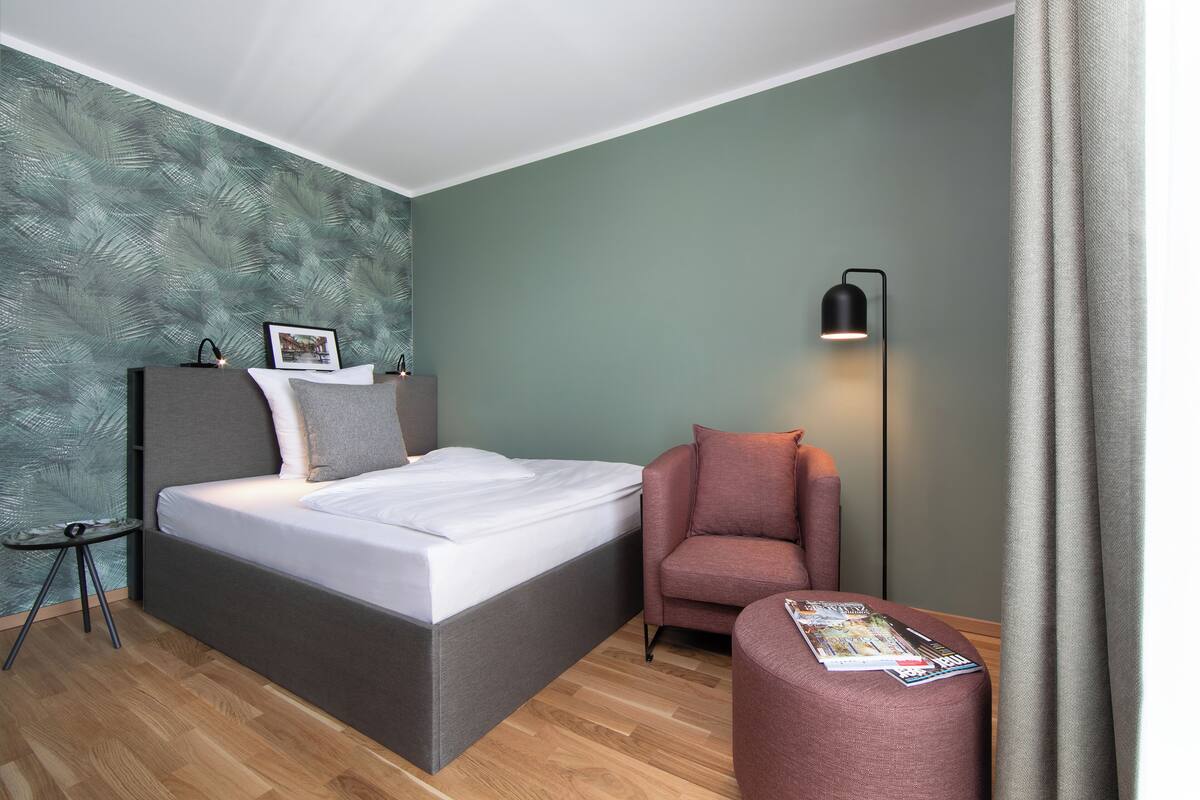A bedroom with a bed, a nightstand, a lamp, a chair, and a magazine on the floor.