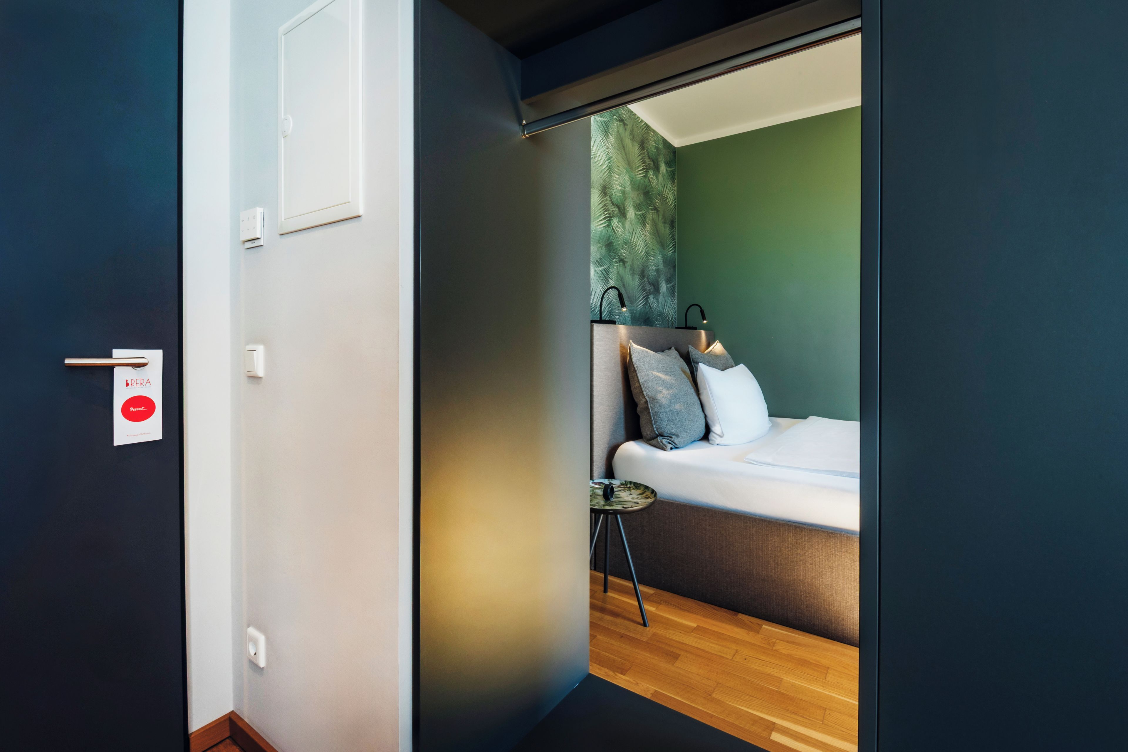 Un dormitorio moderno con cama, almohadas, una mesita y vista a una pared verde.