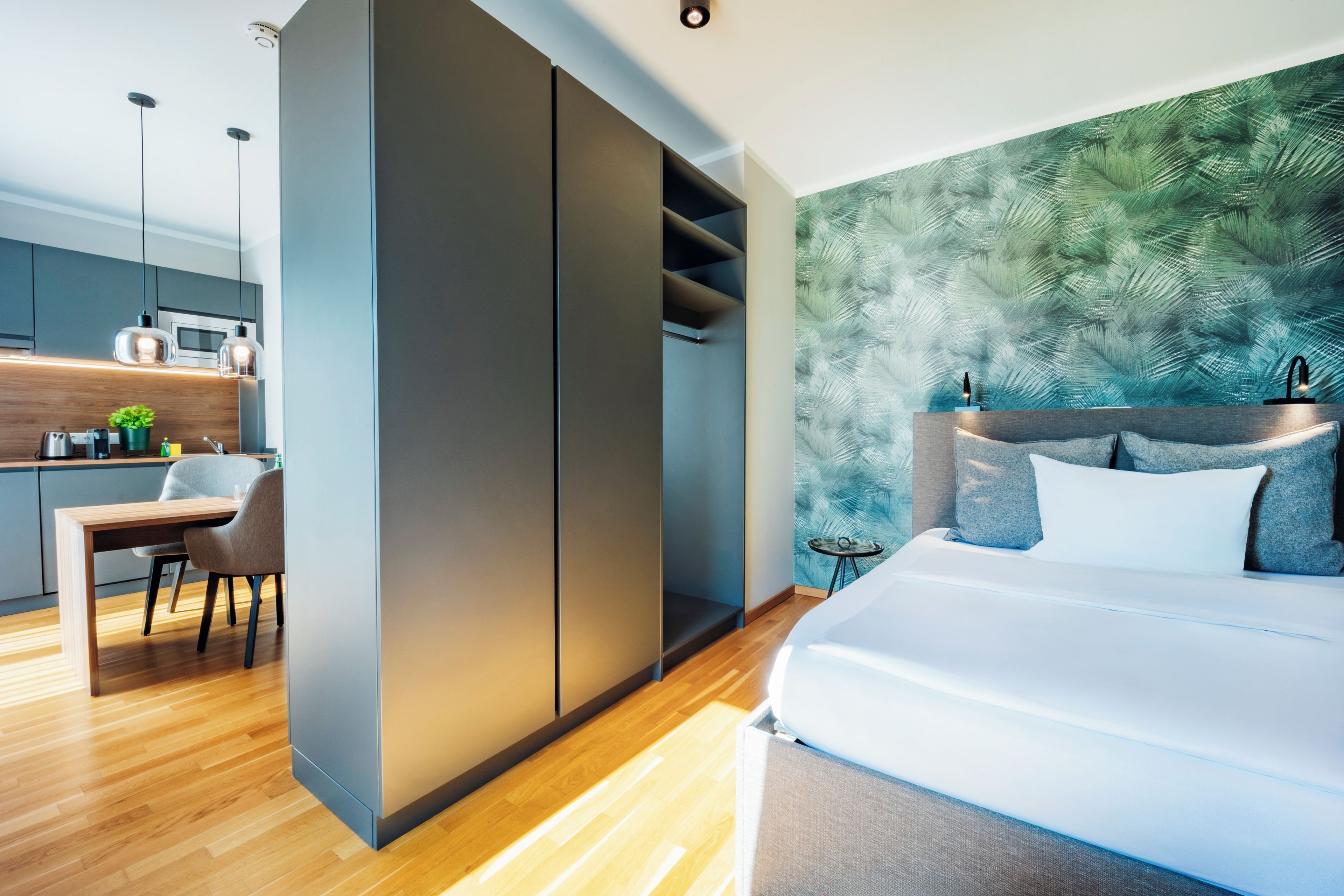 A modern bedroom with a large bed, a nightstand, and a green leaf-patterned wall.