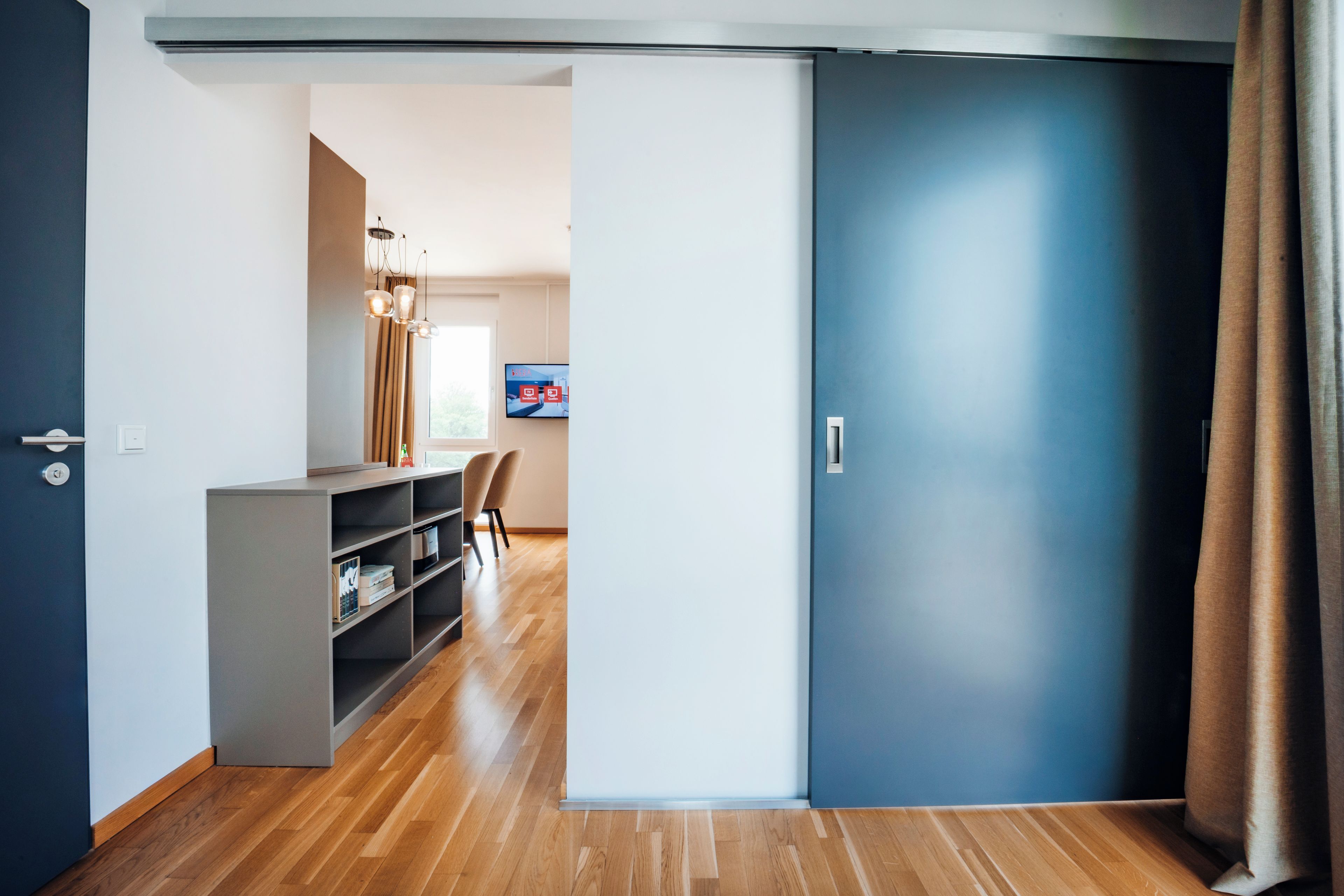 A modern interior with a sliding door, a desk with a chair, and a television on the wall.