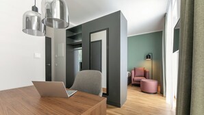 Een moderne woonkamer met een houten salontafel, een grijze fauteuil en een roze poef. Op de tafel staat een laptop, en er is een lamp in de achtergrond zichtbaar.