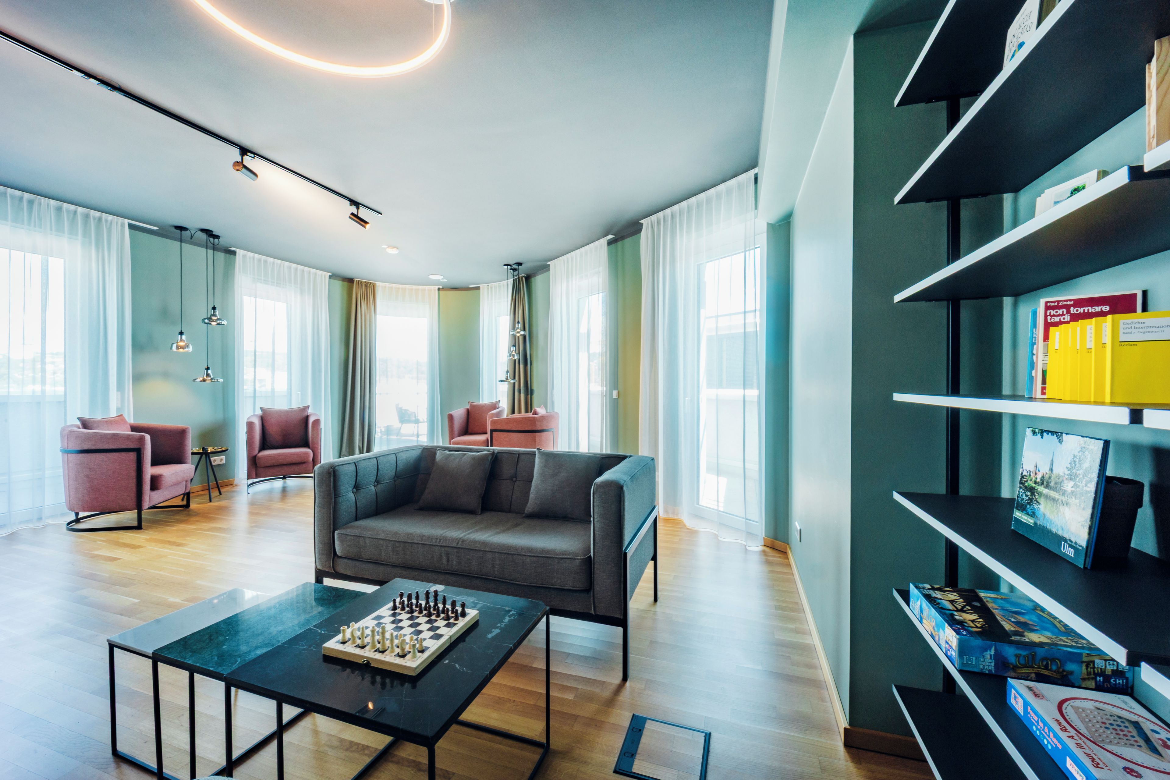 Ein modernes Wohnzimmer mit einer Couch, einem Couchtisch mit einem Schachspiel und einem Bücherregal mit Büchern und Spielen.