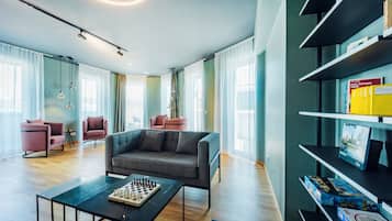 Ein modernes Wohnzimmer mit einer Couch, einem Couchtisch mit einem Schachspiel und einem Bücherregal mit Büchern und Spielen.