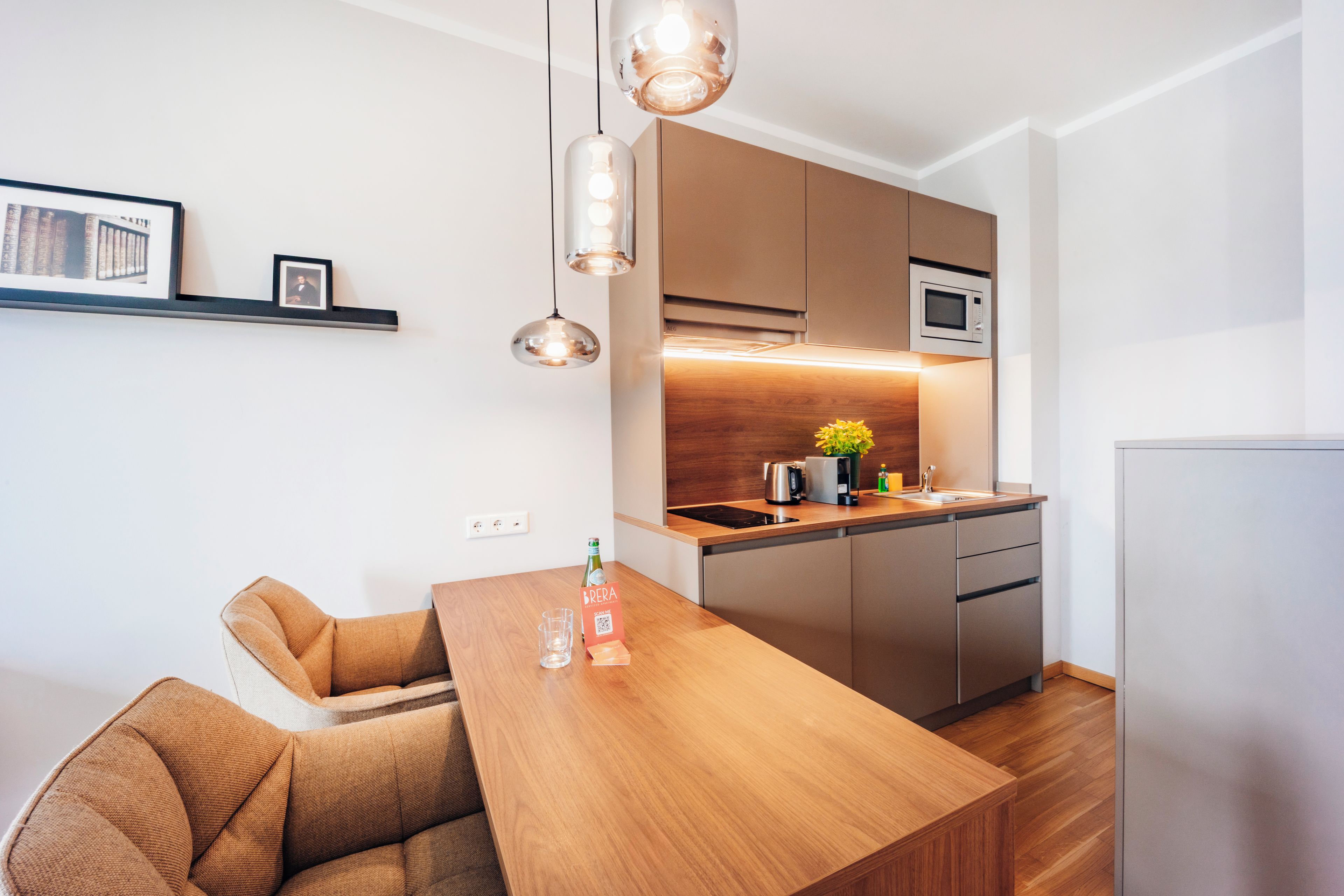 A modern kitchen with a wooden dining table, built-in appliances, and pendant lighting.