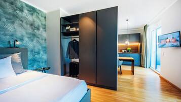 Una habitación de hotel moderna con cama, armario, escritorio y kitchenette.