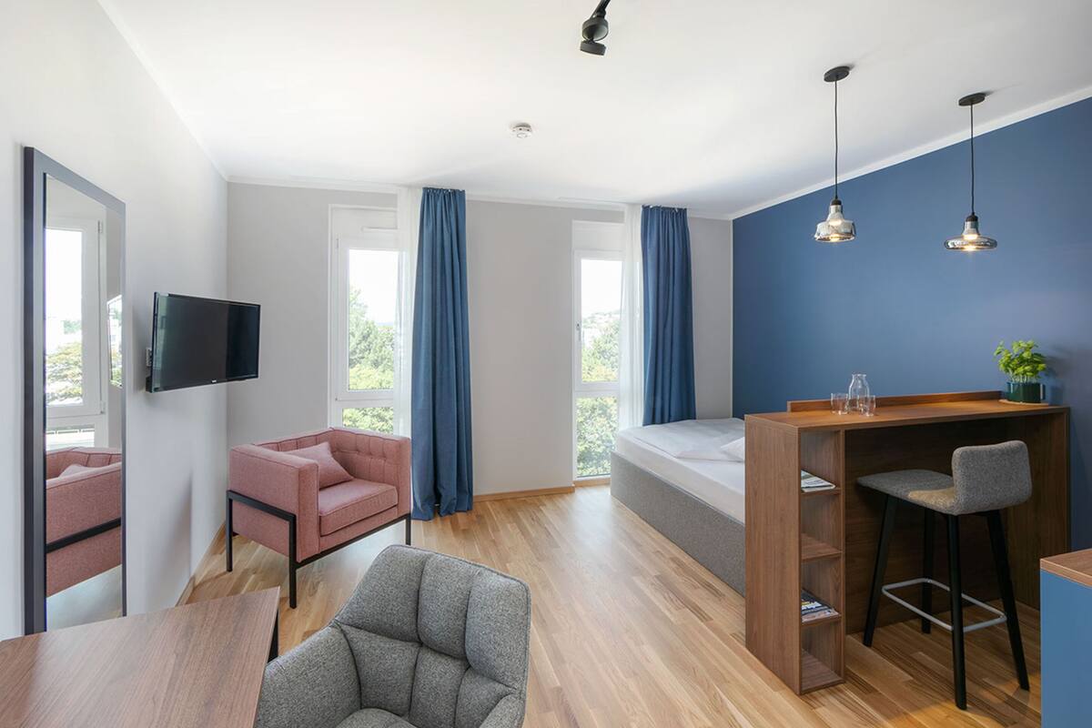 A modern room with a wooden desk, a grey chair, a pink sofa, and a TV mounted on the wall.