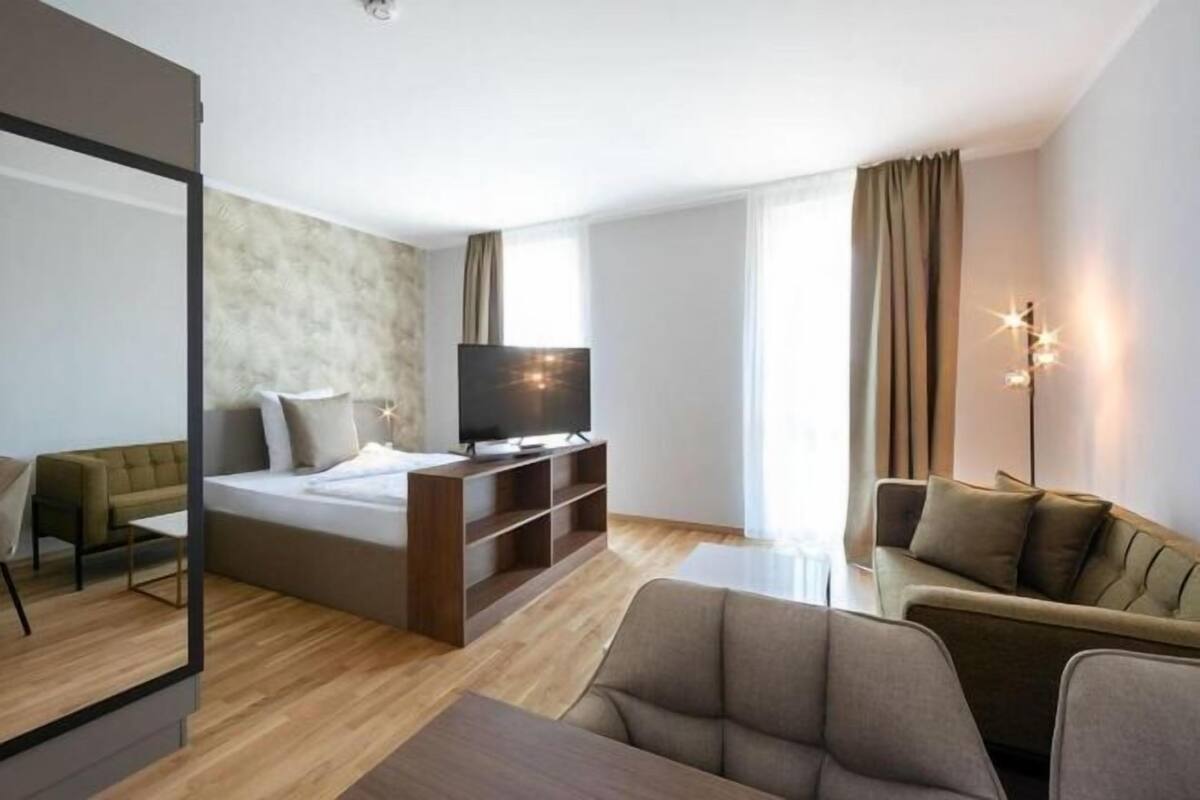 A modern hotel room with a bed, TV, sofa, and a large mirror.