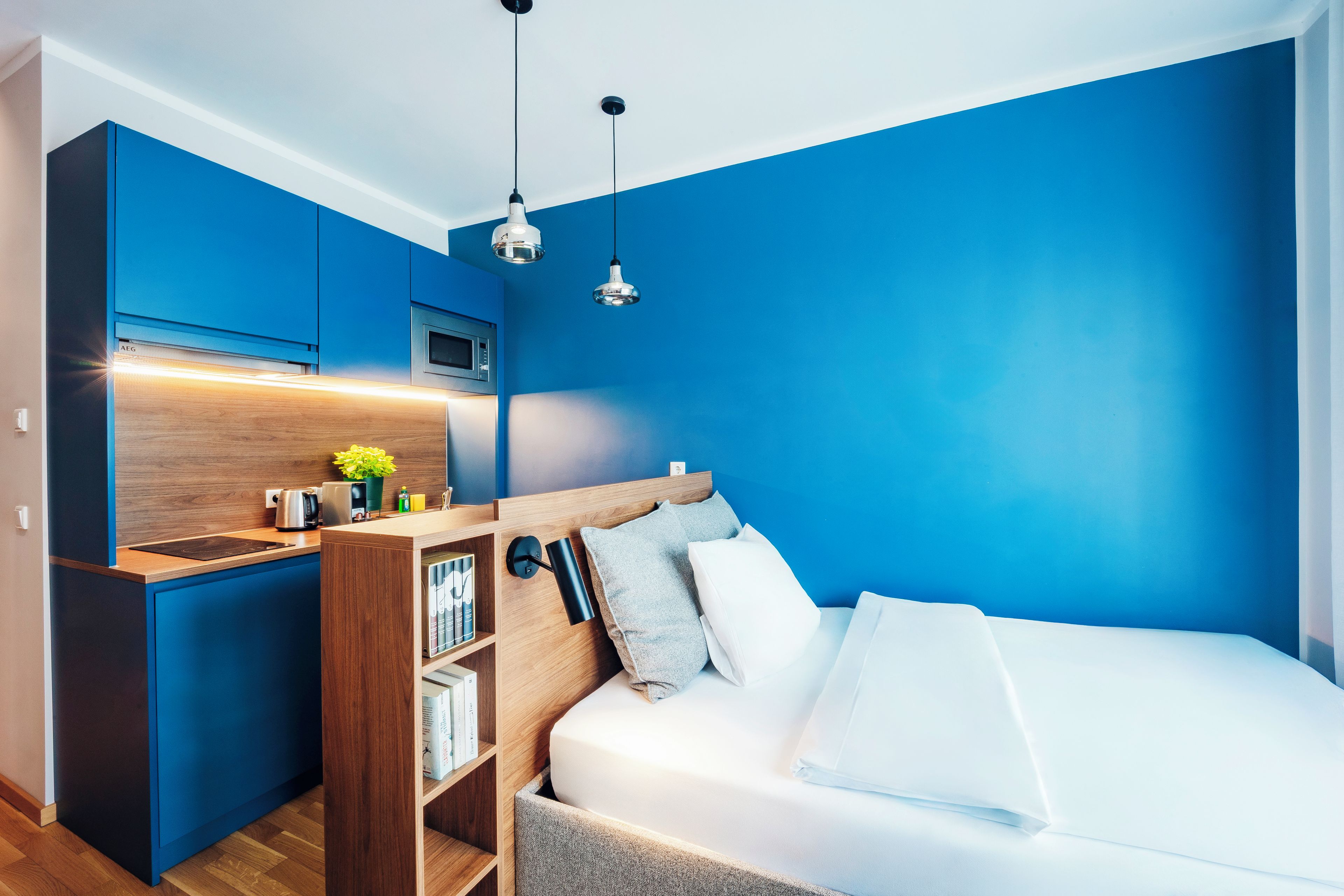 Una camera da letto moderna con angolo cottura integrato, un letto con biancheria bianca e una parete d'accento blu.