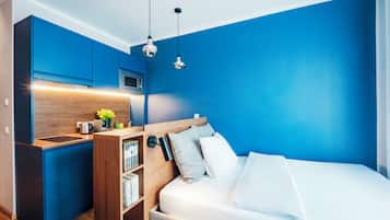 Una camera da letto moderna con angolo cottura integrato, un letto con biancheria bianca e una parete d'accento blu.