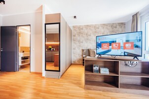 A modern living room with a flat-screen TV, wooden flooring, and a view of a cityscape.