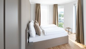 Een moderne slaapkamer met een groot bed, twee ramen voorzien van gordijnen, en uitzicht op de omgeving.