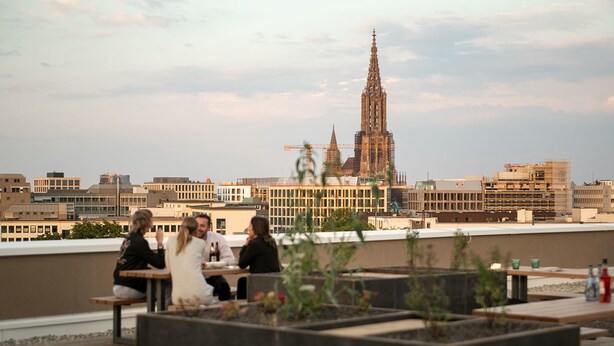 Een terras op het dak met zitplaatsen en uitzicht op een historische kathedraal.