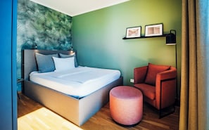 A modern hotel room with a bed, a red armchair, a round ottoman, and a green wall with framed pictures. - Brera Serviced Apartments Ulm (Ulm)