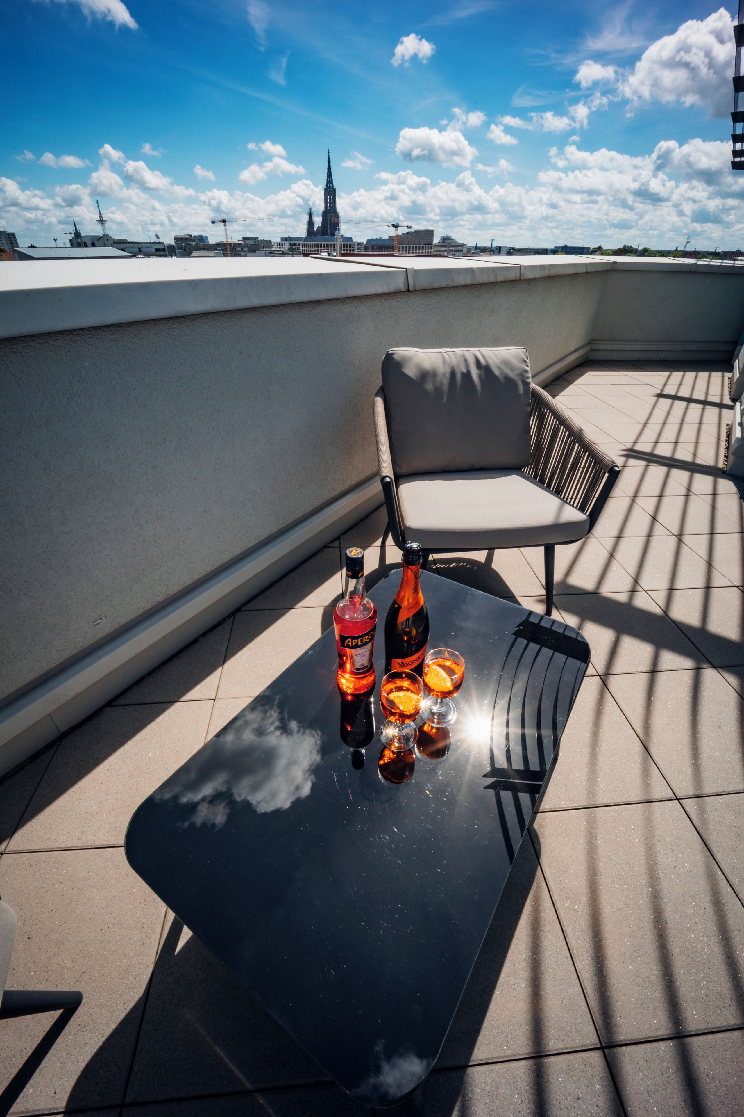 A rooftop terrace with a table, two chairs, and a bottle of Aperol with glasses.