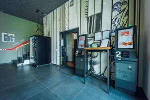 Zona de recepción de un hotel, con mostrador de registro, puertas numeradas y una escalera que conduce a otras plantas.