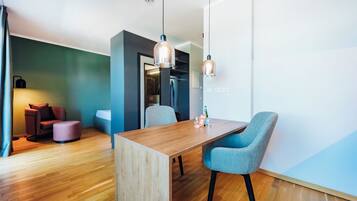 A modern room with a wooden dining table, two blue chairs, a wooden floor, a green accent wall, and pendant lighting.