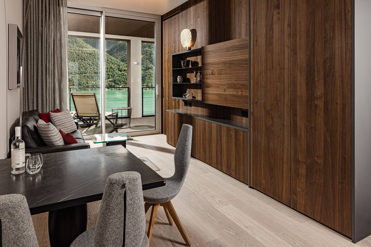 A modern dining area with a dark wooden table, grey upholstered chairs, and a built-in shelf with decorative items.