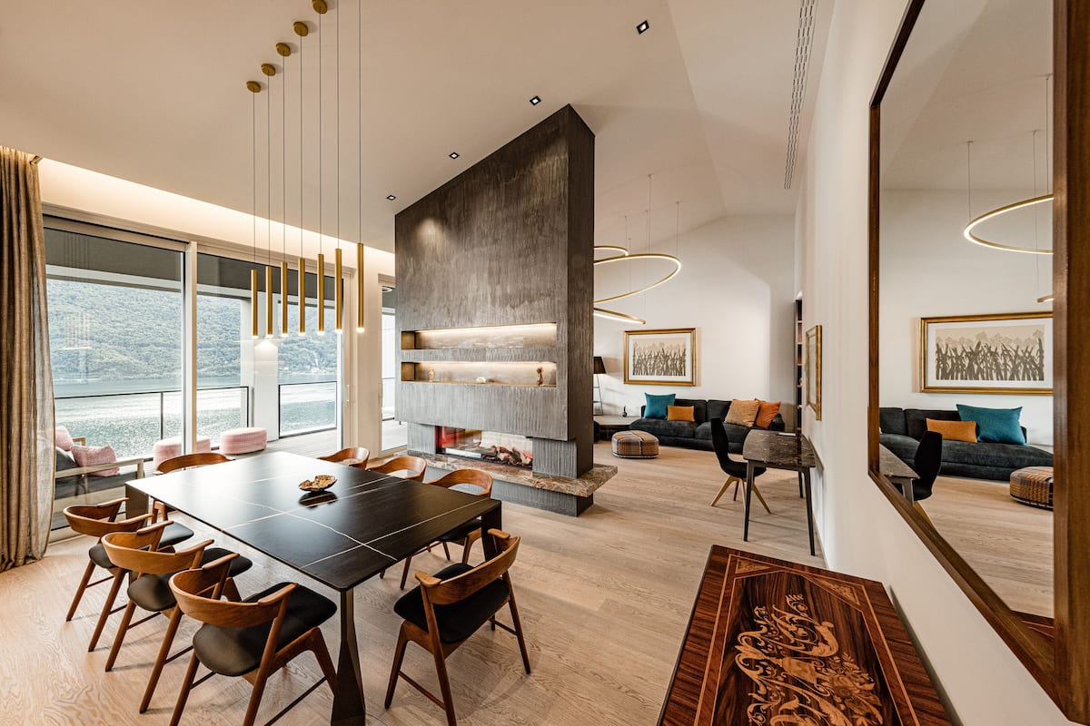 A modern dining area with a long table and chairs, a fireplace, and a sofa in the background.
