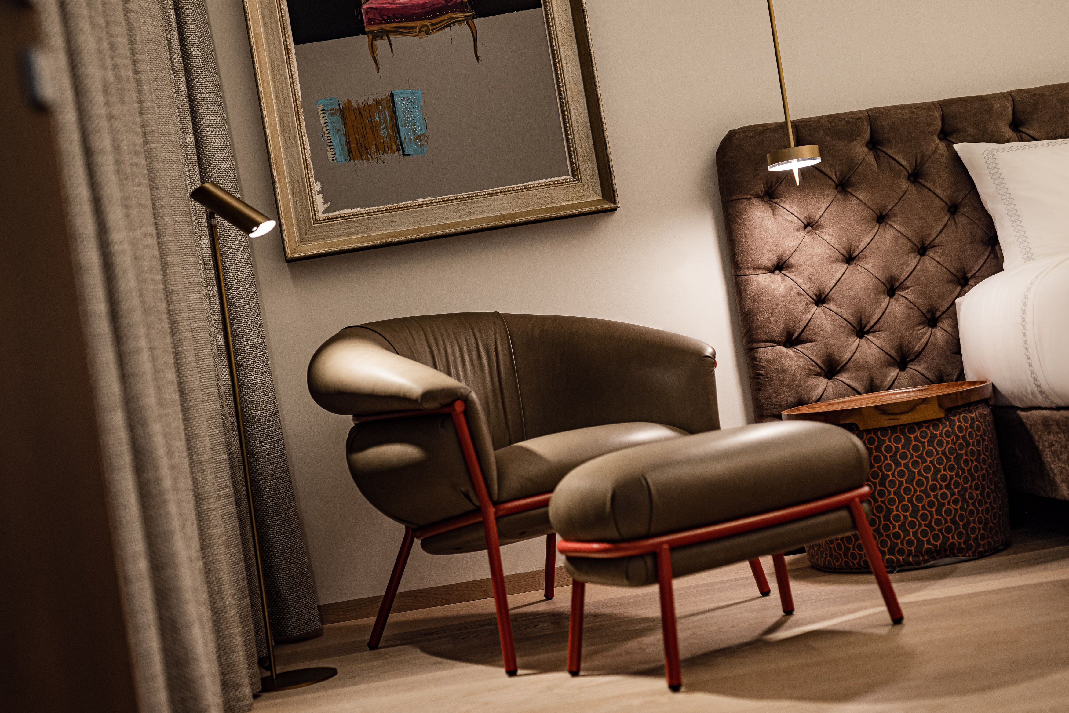 A modern bedroom with a tufted headboard, a leather armchair, a wooden side table, and a floor lamp.