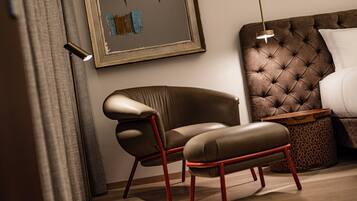 A modern bedroom with a tufted headboard, a leather armchair, a wooden side table, and a floor lamp.