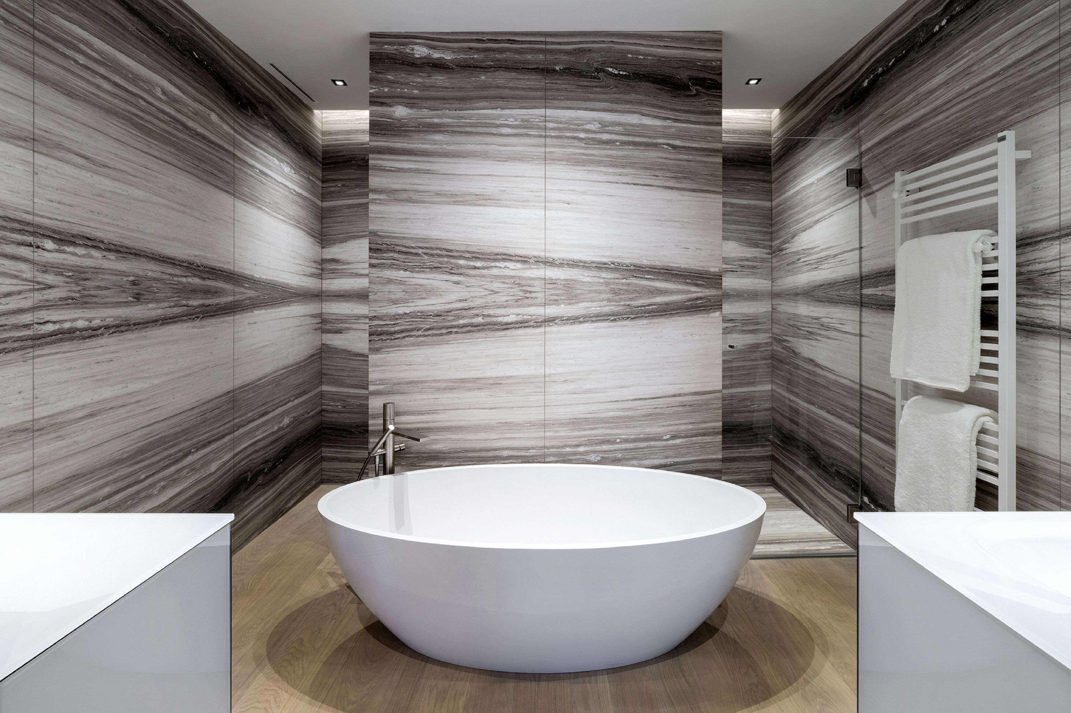 Une salle de bain moderne avec une baignoire sur pieds, des murs en marbre et un porte-serviettes blanc.