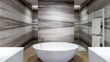 Une salle de bain moderne avec une baignoire sur pieds, des murs en marbre et un porte-serviettes blanc.