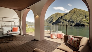 A deck with a sofa, a swing, and a table, overlooking a lake and mountains. - ARIA Retreat & SPA - The Leading Hotels of the World (Porlezza)