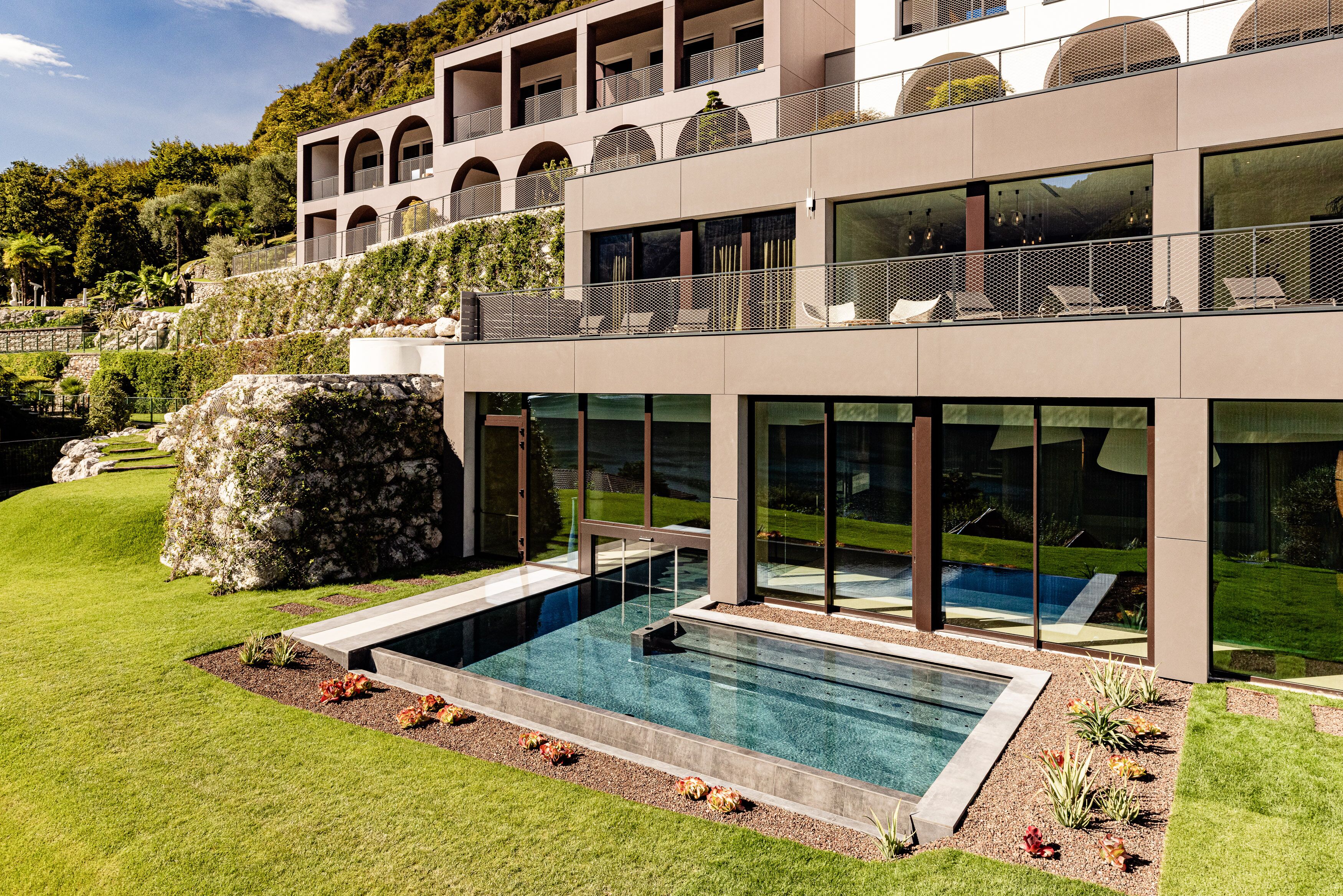 A modern building with a swimming pool, large windows, and a landscaped garden.