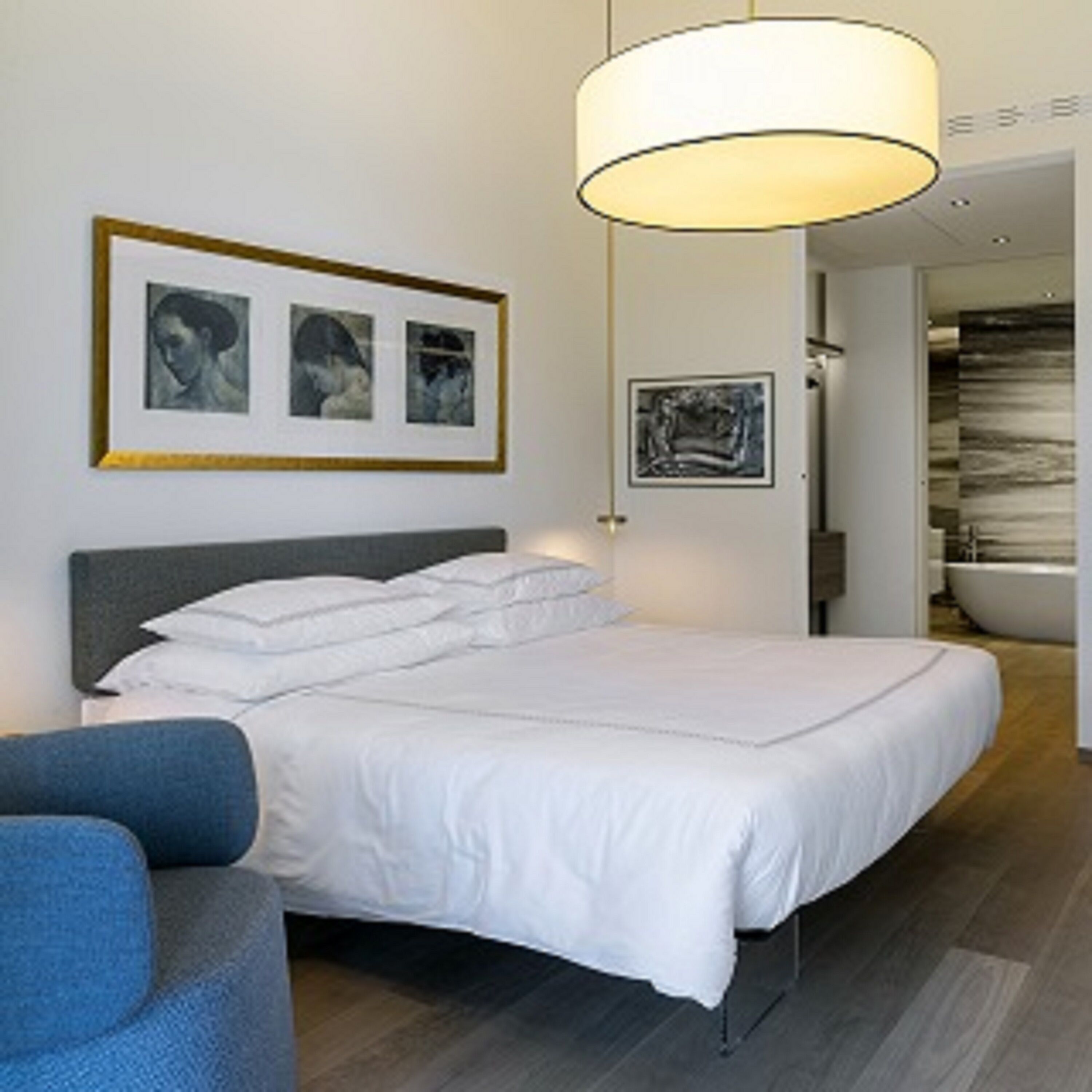Une chambre d’hôtel moderne avec un grand lit, un fauteuil bleu et des œuvres d’art accrochées aux murs.